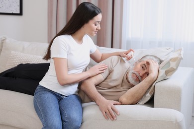 Young woman spraying medication into man's ear at home