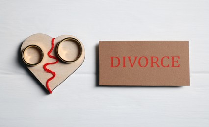 Photo of Divorce concept. Wooden heart with wedding rings and blank card on white table, flat lay