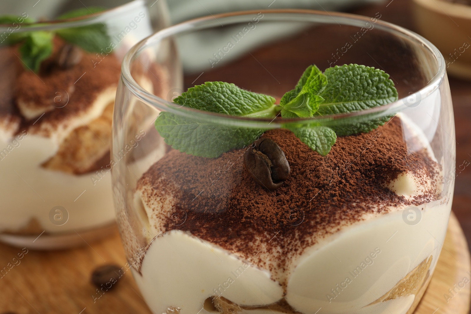 Photo of Delicious tiramisu in glasses, mint leaves and coffee bean on table, closeup