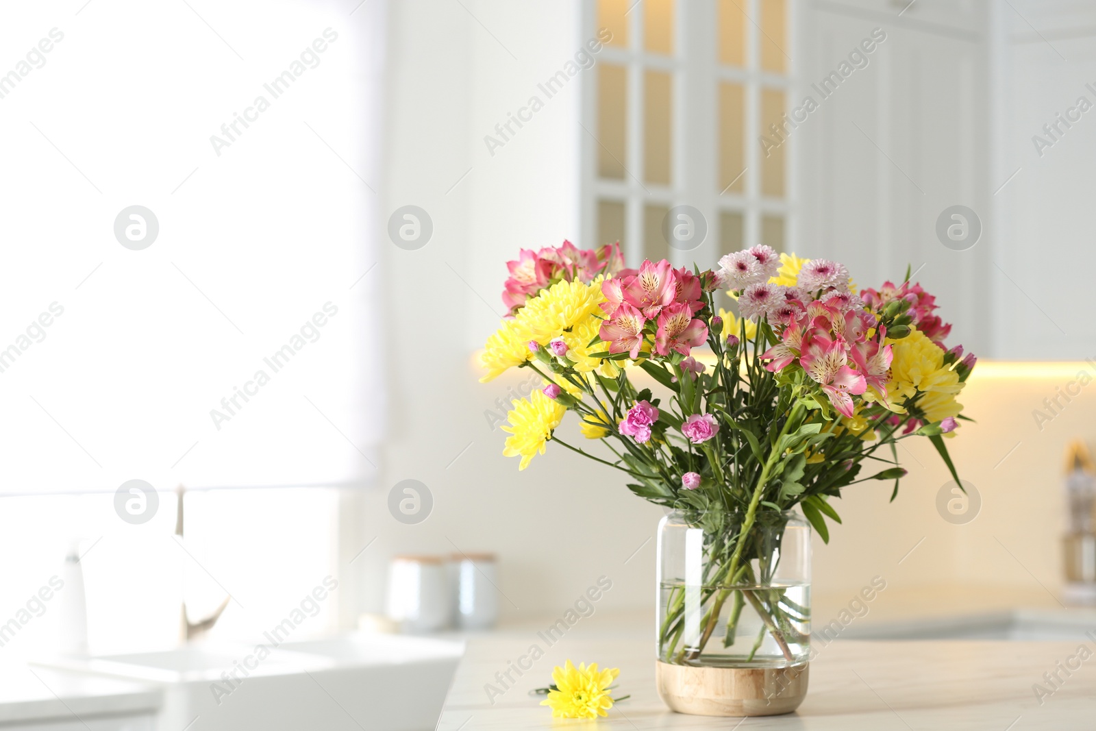 Photo of Vase with beautiful flowers on table in kitchen, space for text. Stylish element of interior design