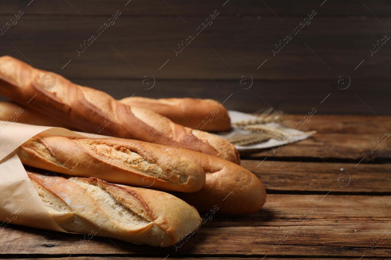 Photo of Fresh tasty baguettes and spikelets on wooden table. Space for text