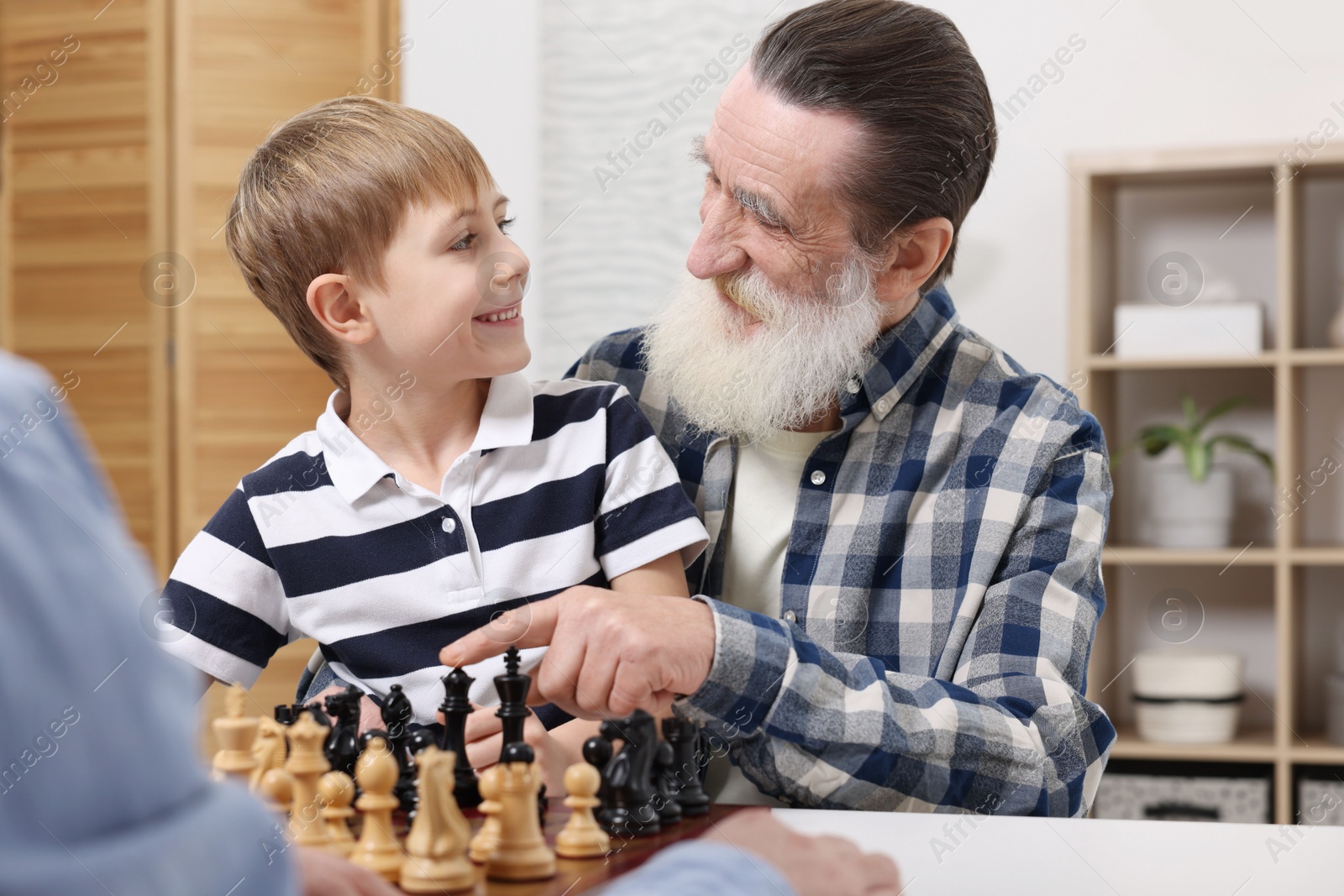 Photo of Family playing chess together at table in room