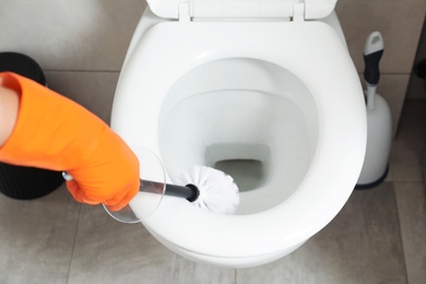 Woman cleaning toilet bowl with brush in bathroom, closeup