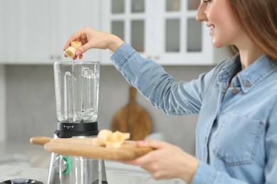 Beautiful young woman adding banana into blender for tasty smoothie in kitchen, closeup
