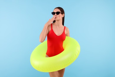 Young woman in stylish swimsuit with inflatable ring on light blue background