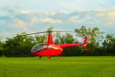 Photo of Modern red helicopter on green grass outdoors