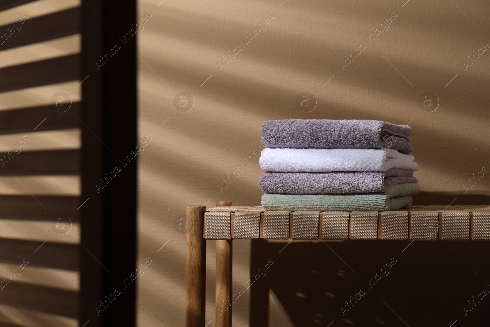 Photo of Stacked terry towels on wicker bench near beige wall, space for text