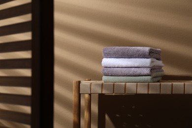 Stacked terry towels on wicker bench near beige wall, space for text