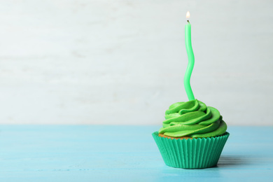 Photo of Delicious birthday cupcake with cream and burning candle on blue wooden table. Space for text