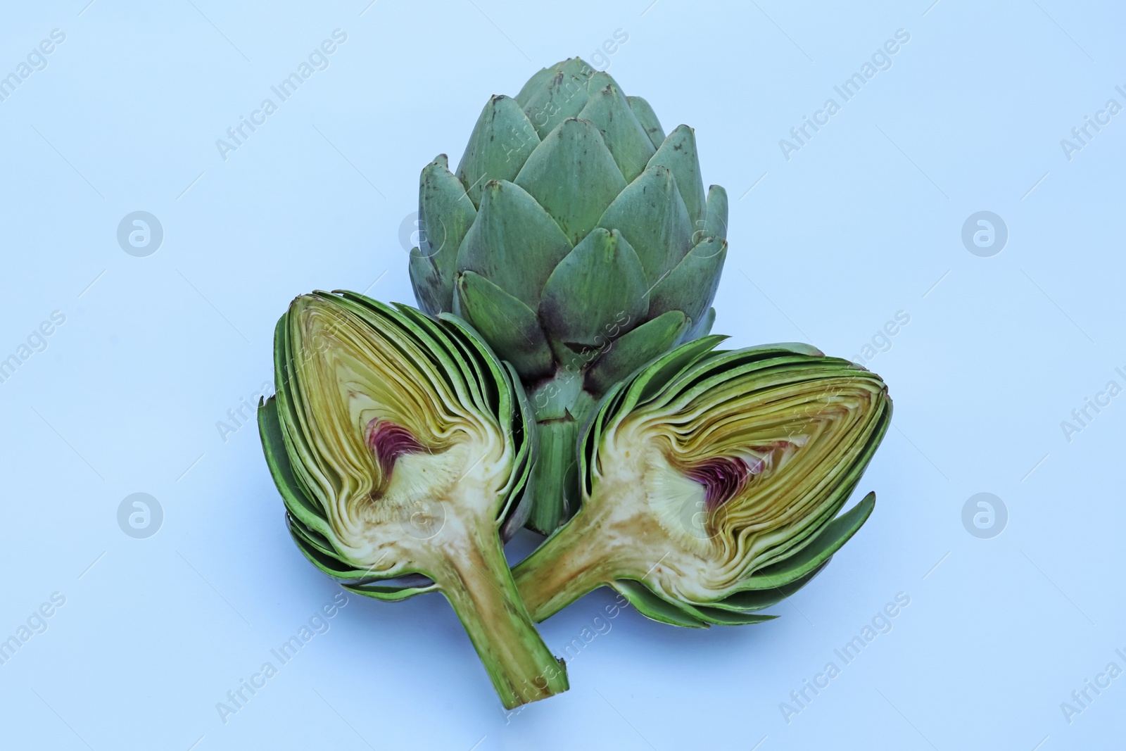 Photo of Cut and whole fresh raw artichokes on light blue background, flat lay