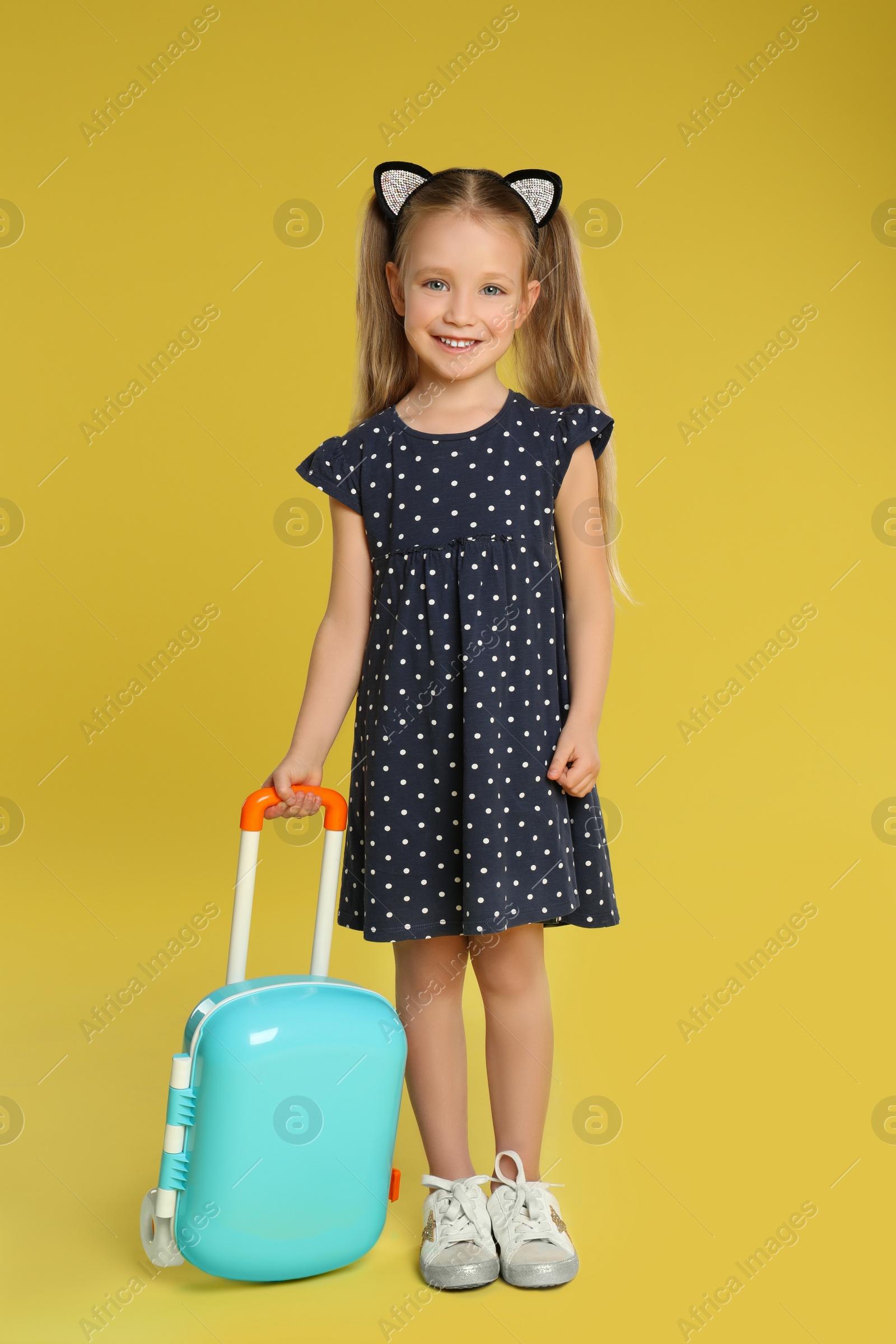 Photo of Cute little girl with suitcase on yellow background