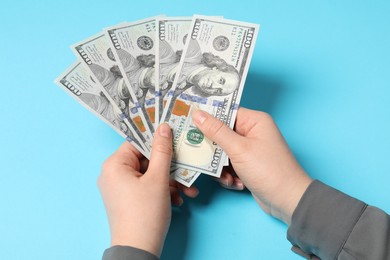 Money exchange. Woman holding dollar banknotes on light blue background, above view