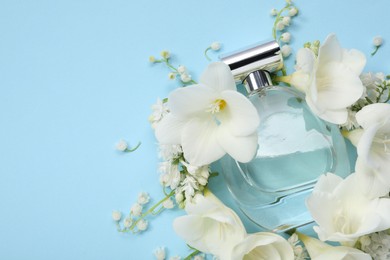 Photo of Luxury perfume and floral decor on light blue background, flat lay. Space for text