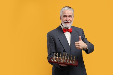 Photo of Man with chessboard and game pieces showing thumbs up on orange background, space for text