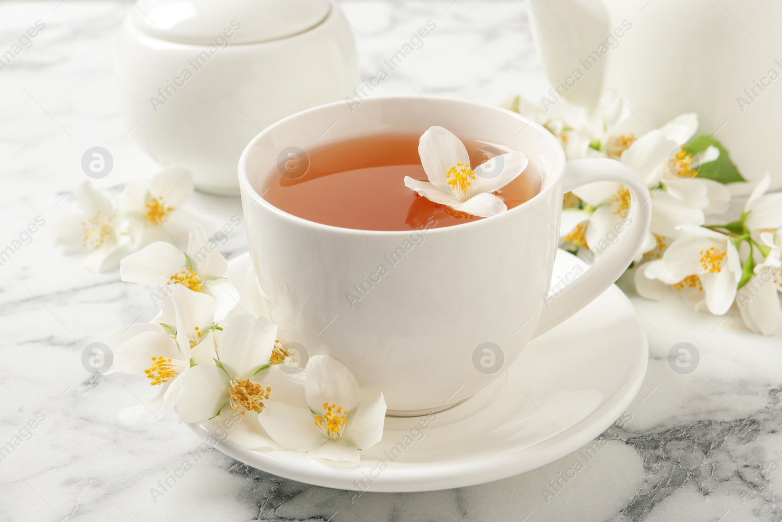 Photo of Cup of aromatic jasmine tea and fresh flowers on white marble table