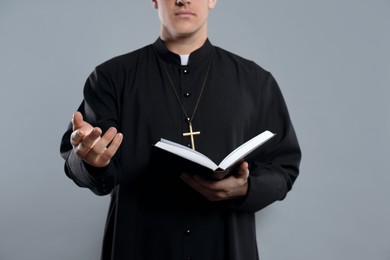 Priest with Bible on grey background, closeup