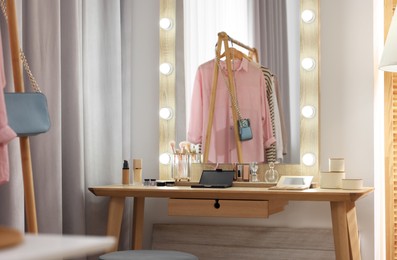 Photo of Makeup room. Stylish mirror and different beauty products on wooden dressing table indoors