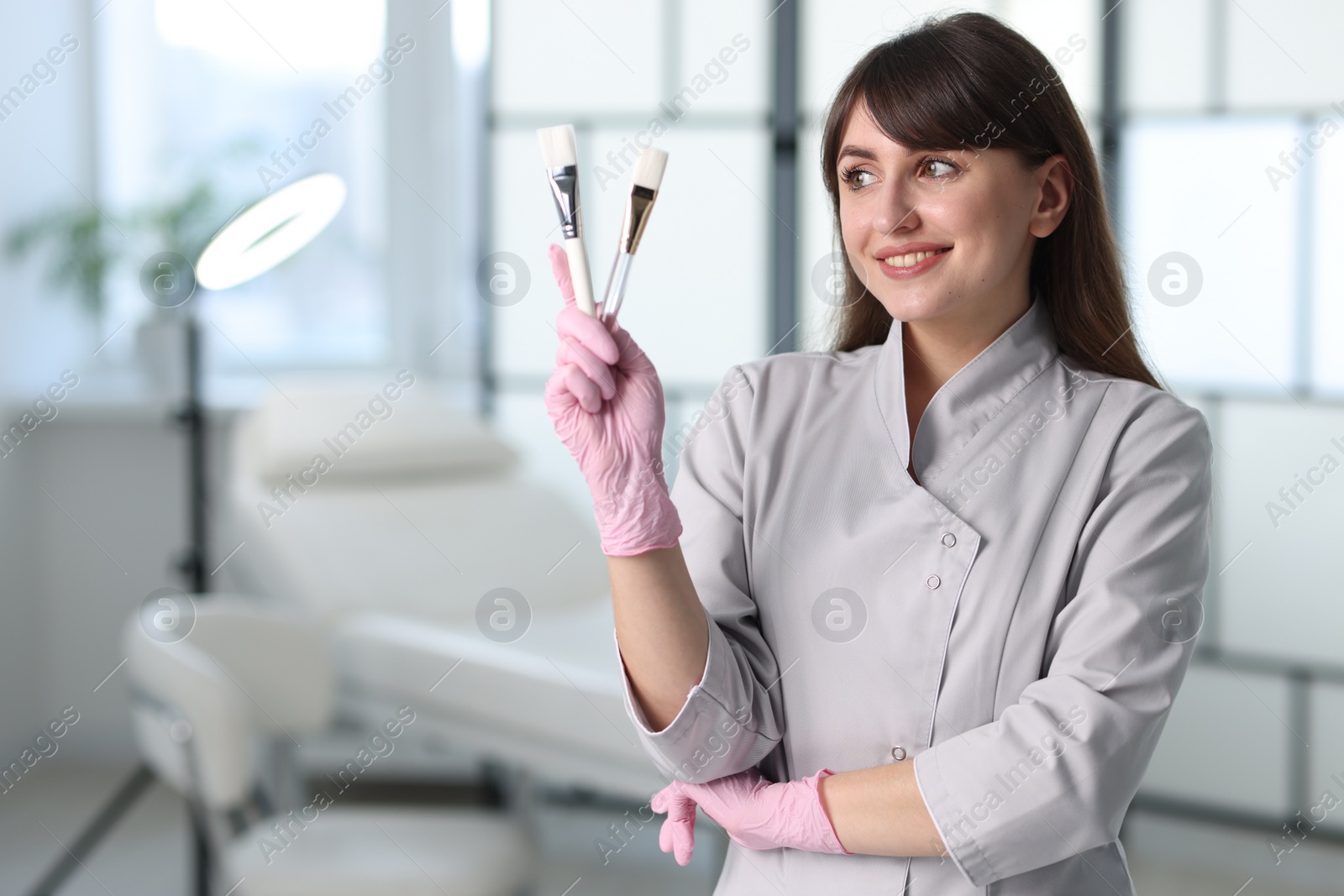 Photo of Cosmetologist with cosmetic brushes in clinic, space for text