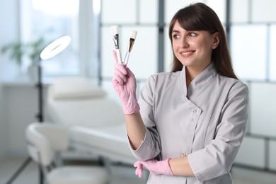 Cosmetologist with cosmetic brushes in clinic, space for text