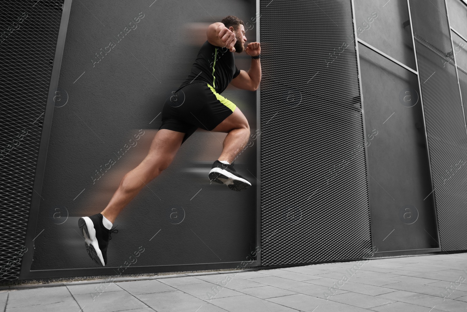 Image of Sporty young man running on street, low angle view. Motion blur effect showing his speed