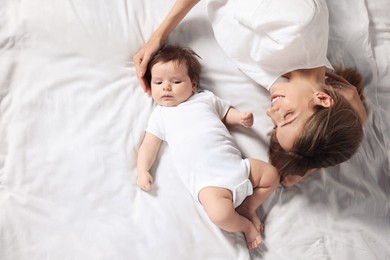 Photo of Mother and her little baby lying on bed, top view. Space for text