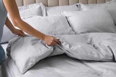Woman putting soft blanket on bed with pillows, closeup