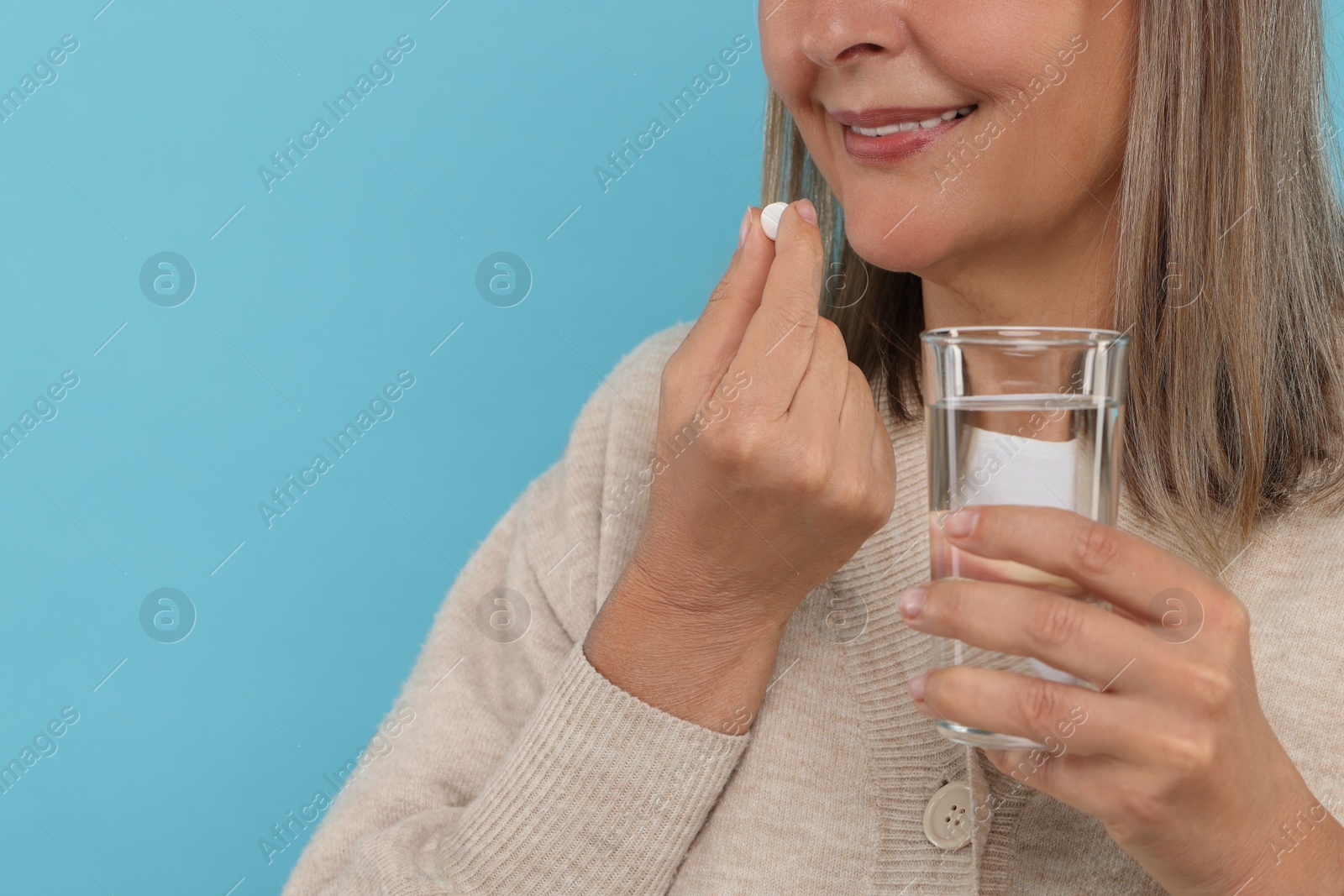 Photo of Senior woman with glass of water taking pill on light blue background, closeup