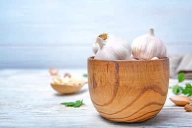 Photo of Wooden bowl with fresh garlic bulbs on table