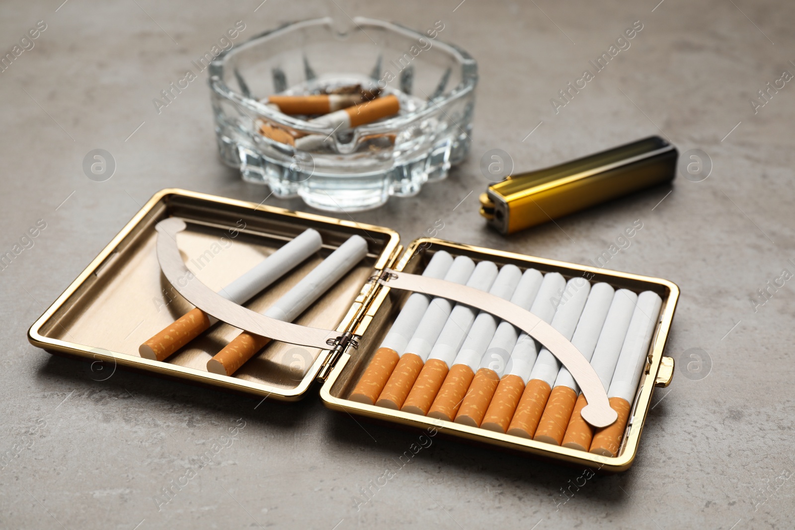 Photo of Open case with tobacco filter cigarettes, lighter and glass ashtray on grey table