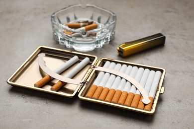 Open case with tobacco filter cigarettes, lighter and glass ashtray on grey table