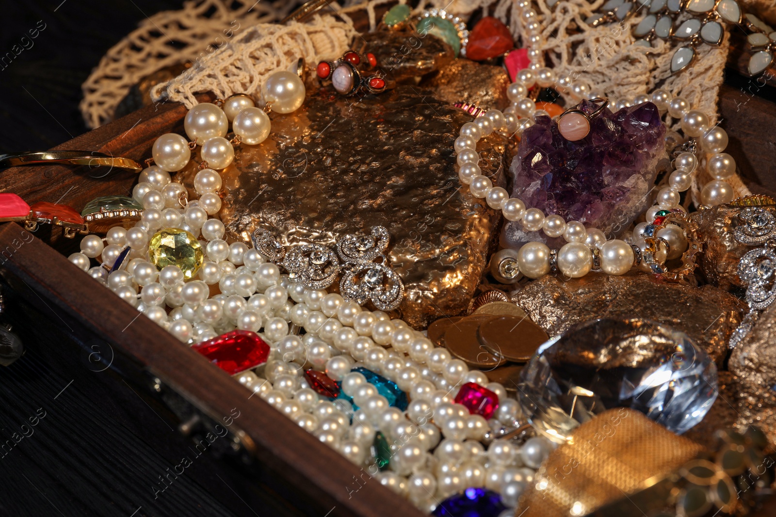 Photo of Gold nuggets, jewelry and gemstones in treasure chest, closeup