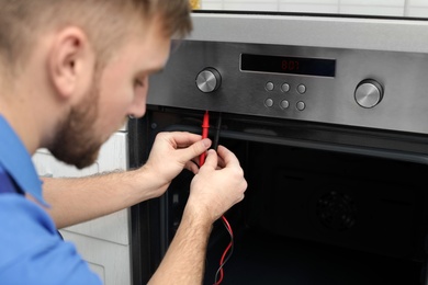 Professional serviceman repairing modern oven in kitchen