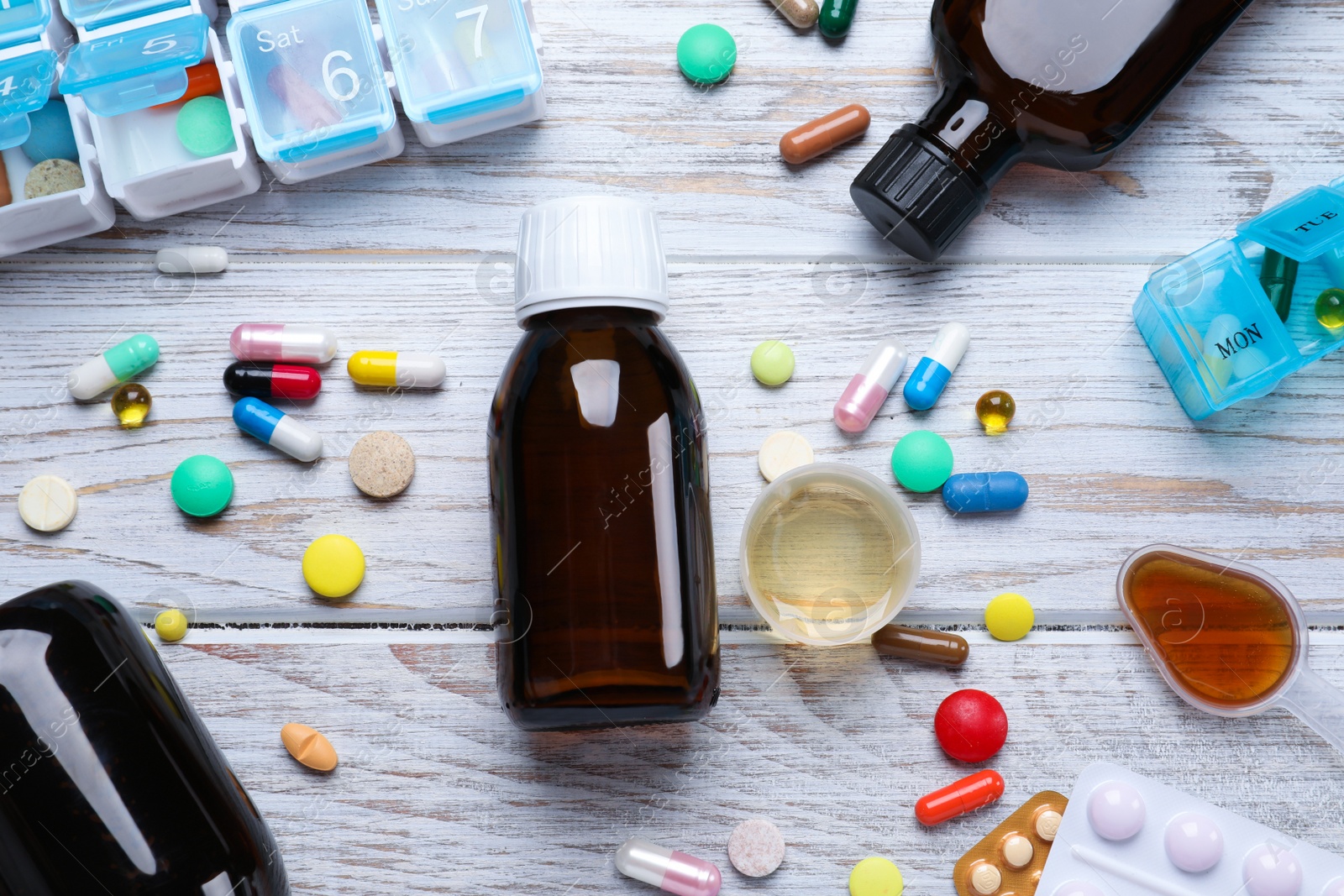 Photo of Flat lay composition with bottles of syrup, measuring cup and pills on white wooden table. Cold medicine