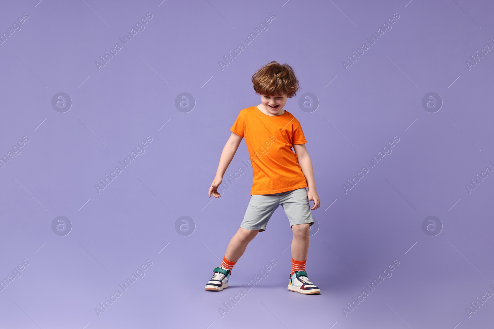 Photo of Happy little boy dancing on violet background