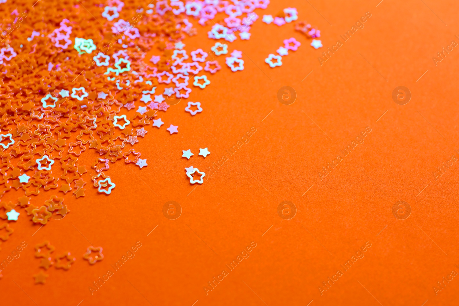 Photo of Shiny bright star shaped glitter on orange background. Space for text