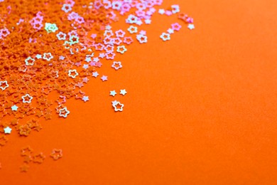 Photo of Shiny bright star shaped glitter on orange background. Space for text