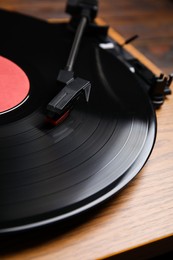 Photo of Modern vinyl record player with disc on table, closeup