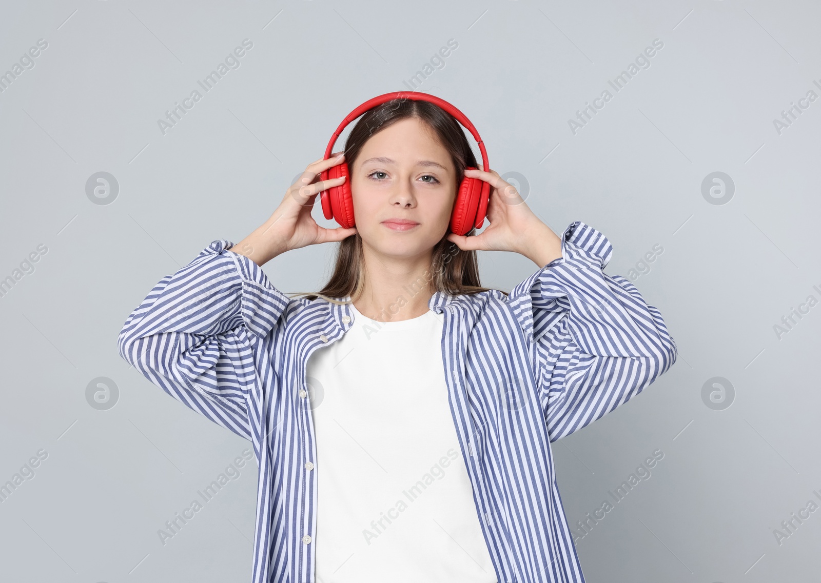 Photo of Teenage girl listening to music with red headphones on light grey background