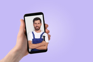 Find plumber. Man using mobile phone on light violet background, closeup. Specialist looking out of gadget