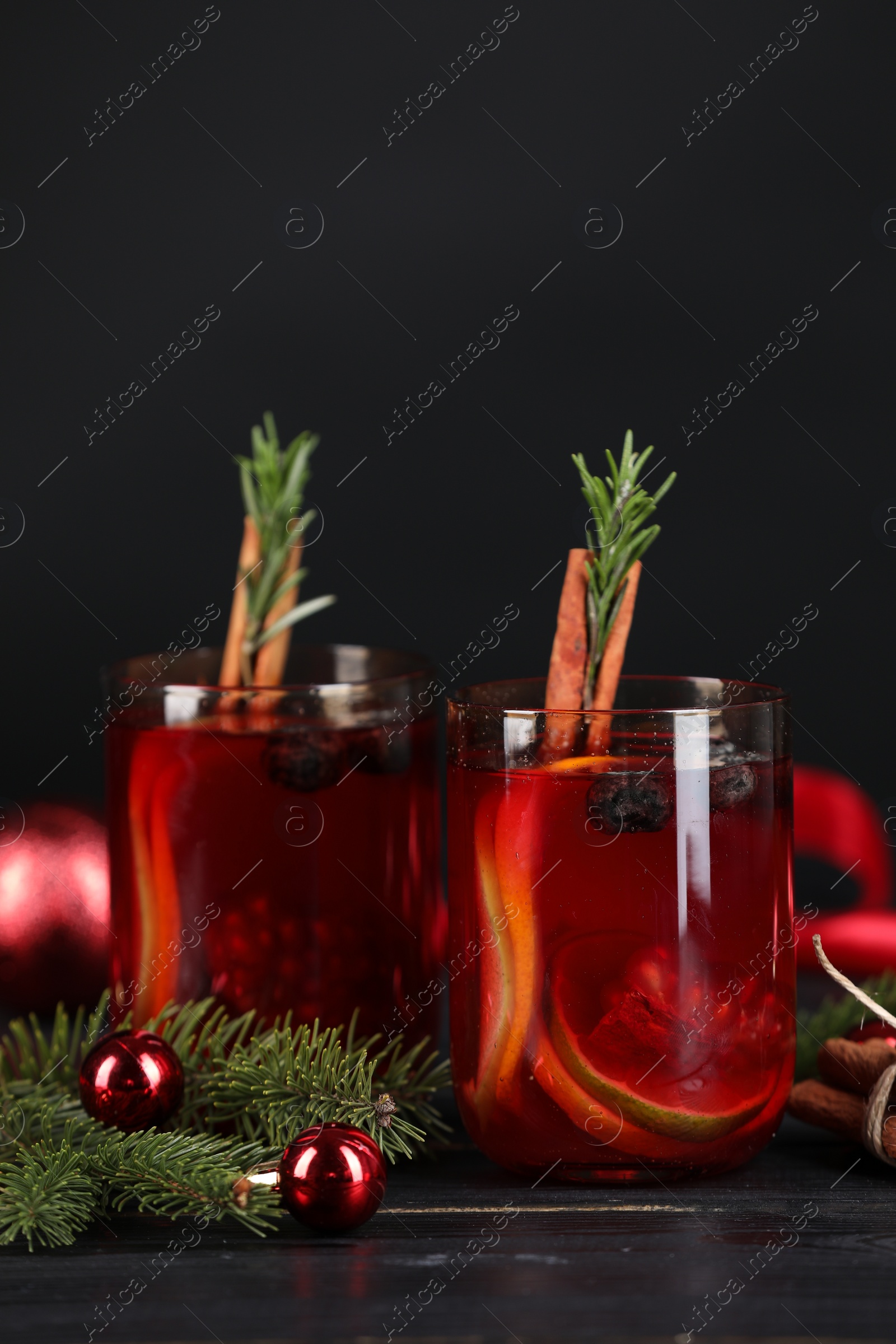 Photo of Aromatic Sangria drink in glasses, ingredients and Christmas decor on black wooden table