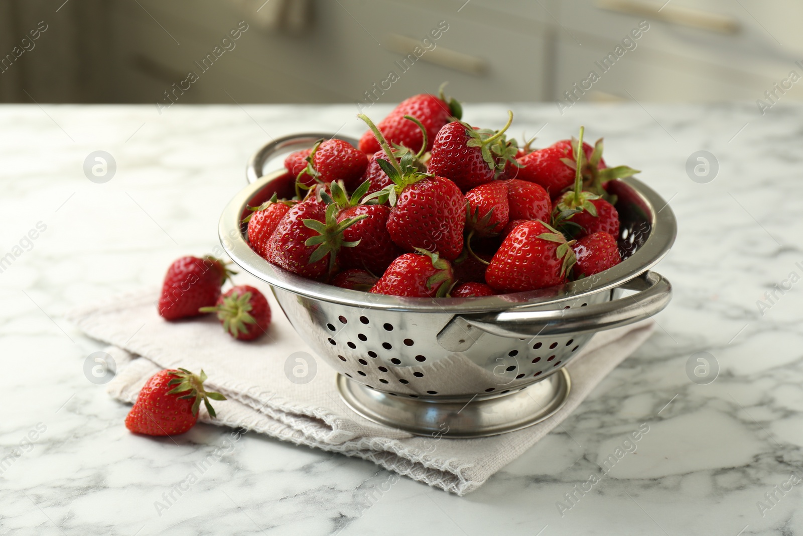 Photo of Metal colander with fresh strawberries on white marble table indoors