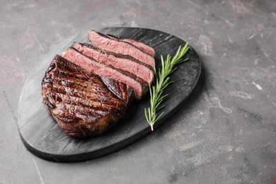 Delicious fried beef meat with rosemary on grey textured table, space for text