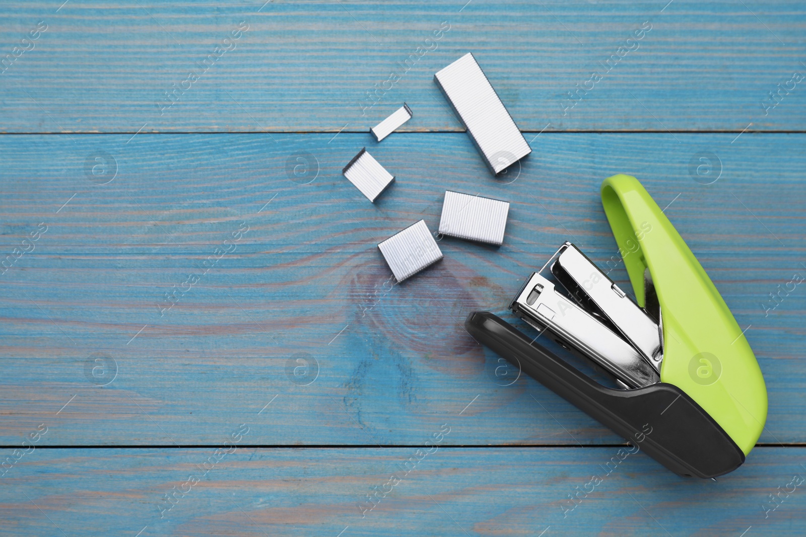 Photo of New bright stapler with staples on light blue wooden table, fat lay. Space for text