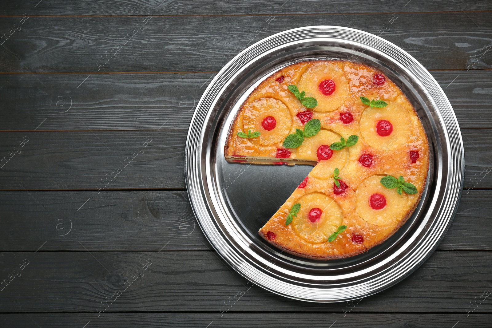 Photo of Delicious cut pineapple pie with cherry and mint on black wooden table, top view. Space for text