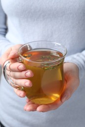 Photo of Woman holding cup of tasty herbal tea with thyme, closeup