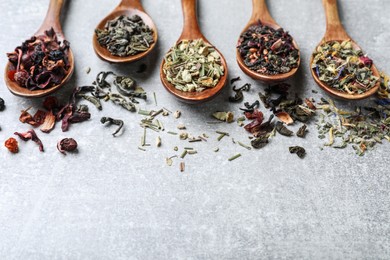 Composition with different teas and spoons on light grey stone table. Space for text