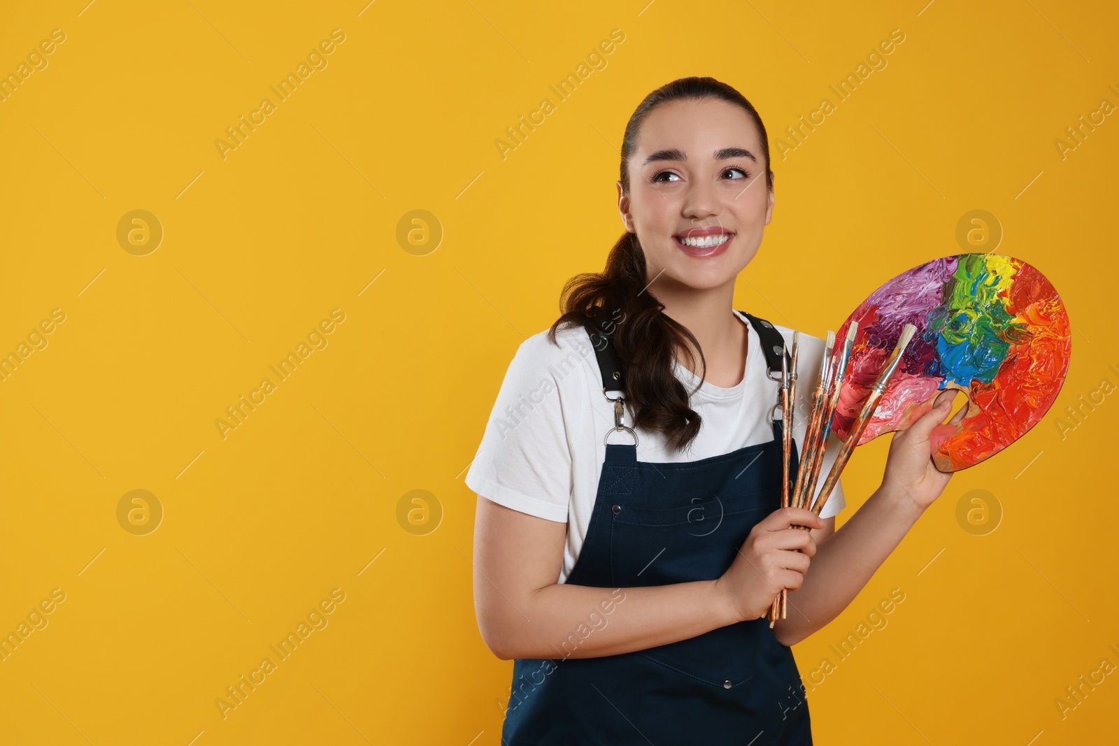 Photo of Woman with painting tools on yellow background, space for text. Young artist