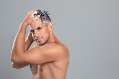 Handsome man washing hair on grey background, space for text