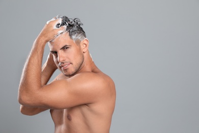 Photo of Handsome man washing hair on grey background, space for text