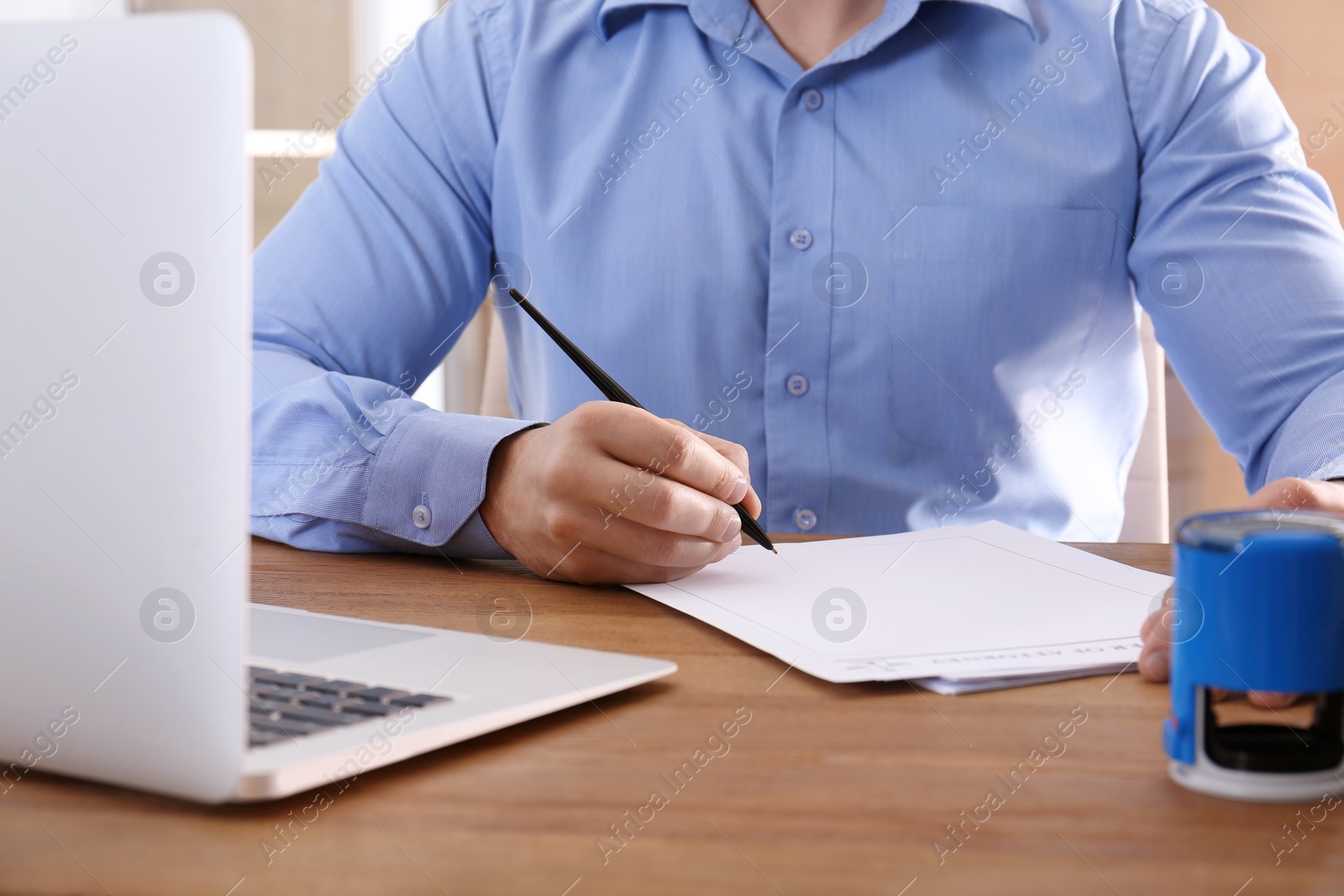 Photo of Male notary signing document at table indoors, closeup